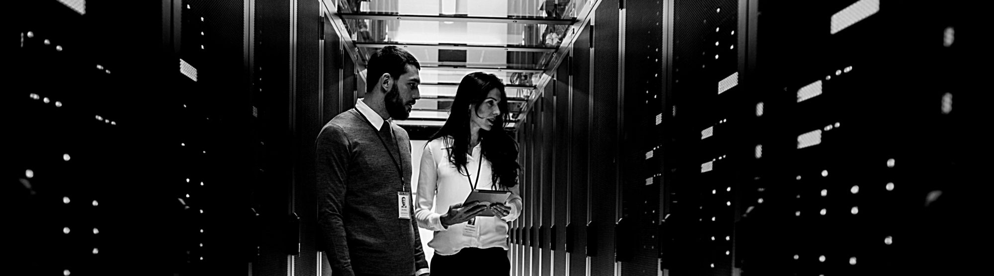 image of two professional workers, a man and woman, standing in front of data center cabinents with clipboards